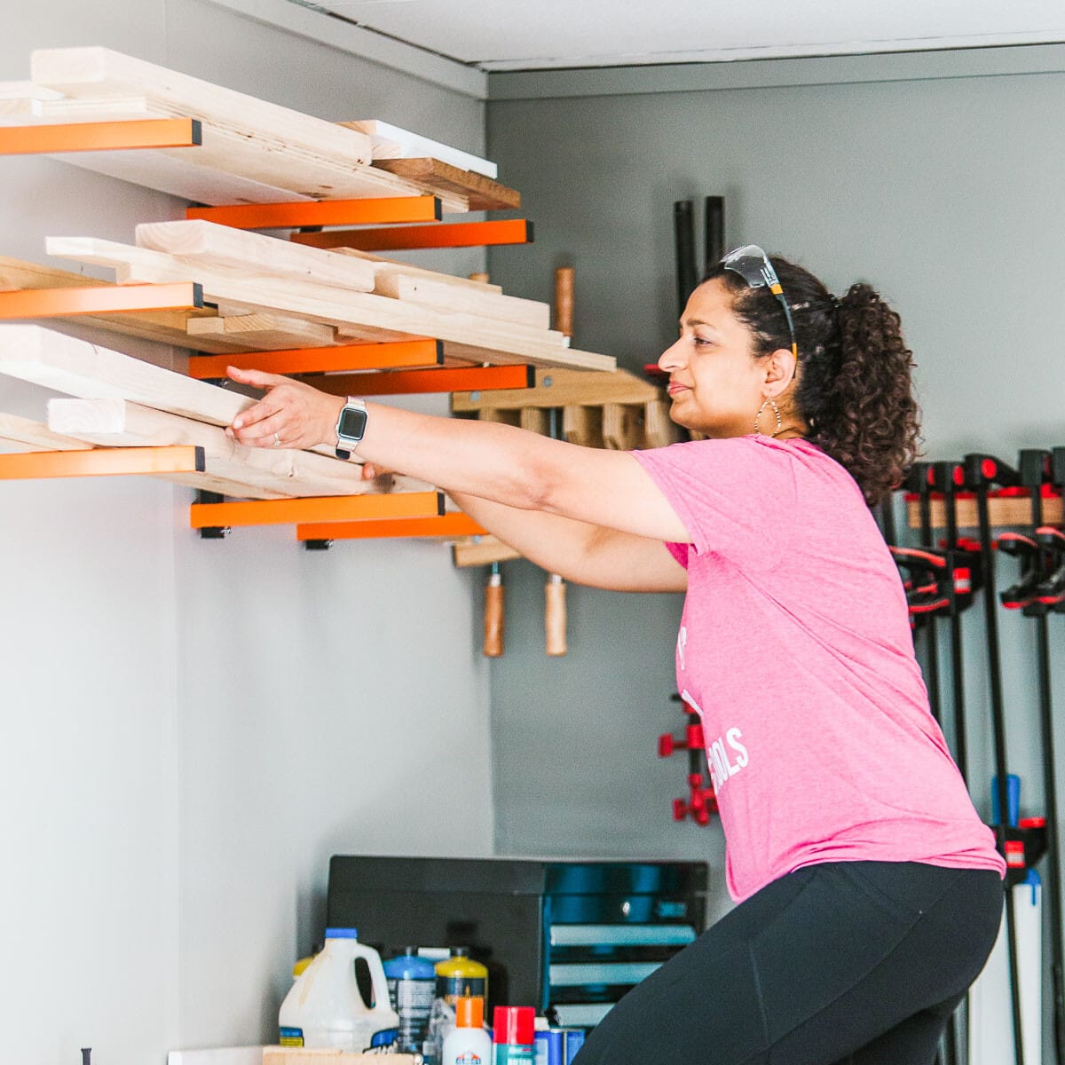 woman taking down lumber from racks in workshop