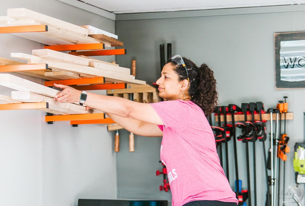 woman putting lumber on a wall mounted lumber rack