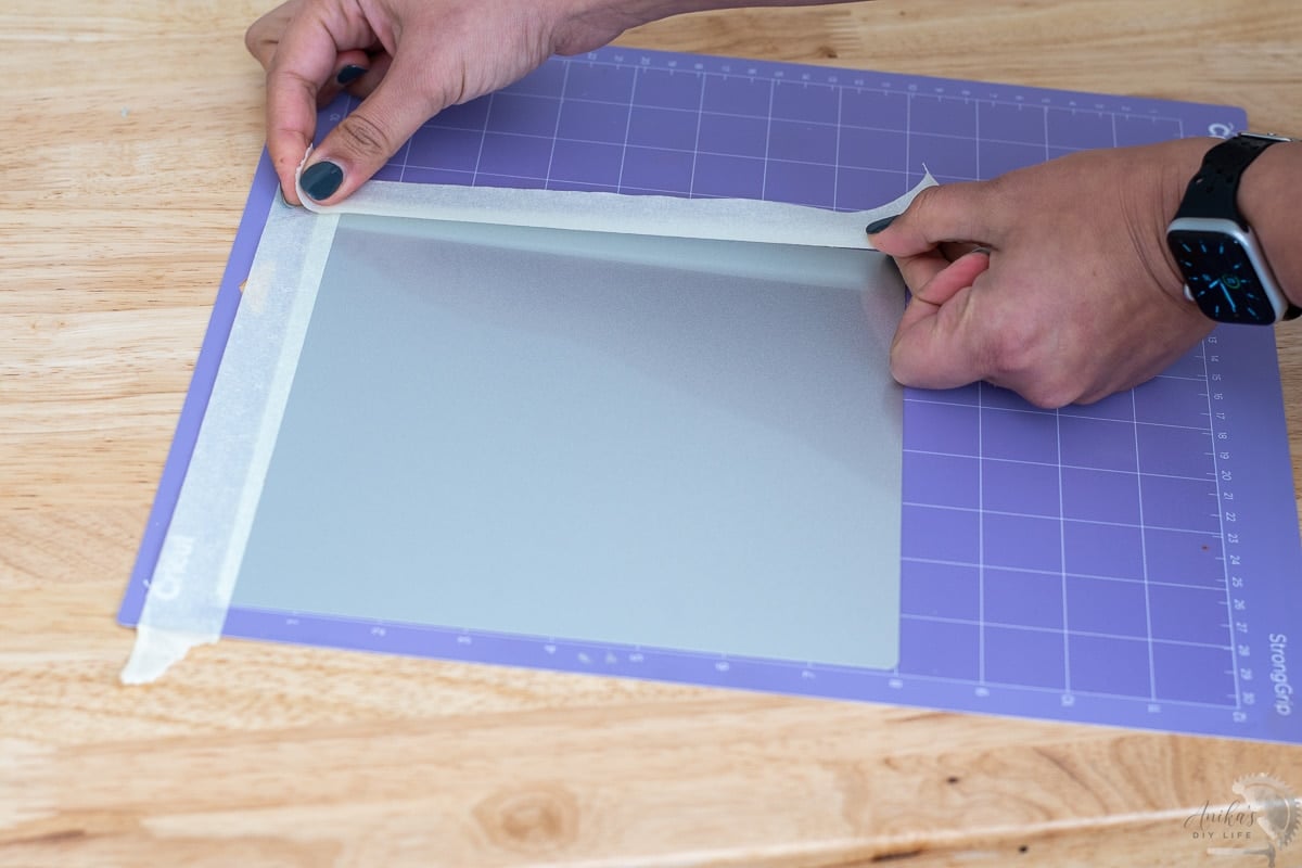 applying tape to hold the blank in place on the mat to engrave on Cricut Maker