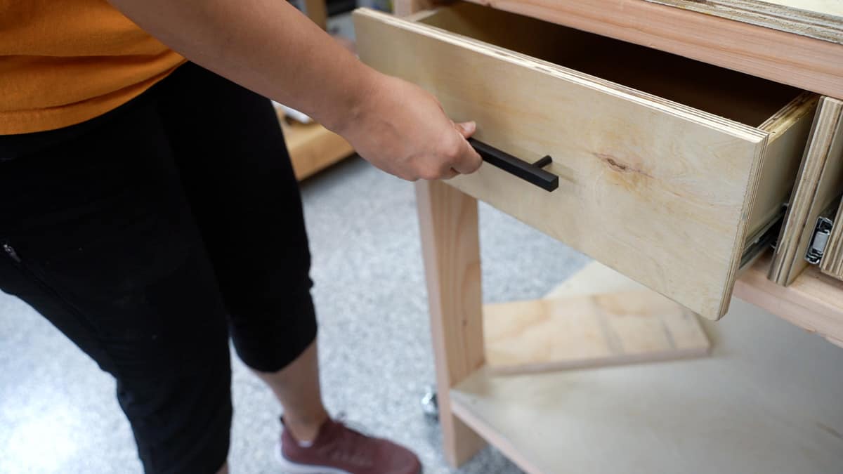 Woman attaching drawer pulls to the drawer in the workbench