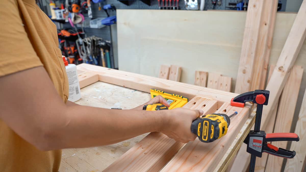 Woman attaching 2x4s to build the legs for the workbench