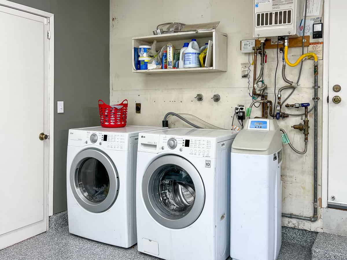 Laundry area in garage with messy plumbing and blank wall.