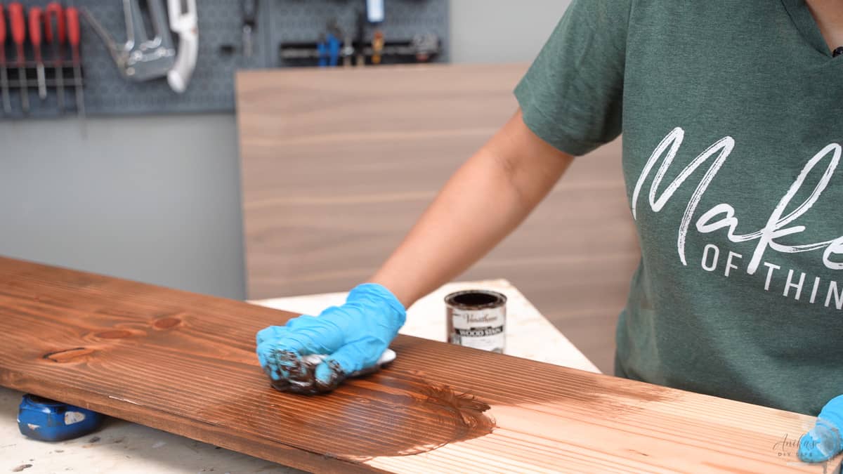woman applying dark stain on pine board in circular motion.