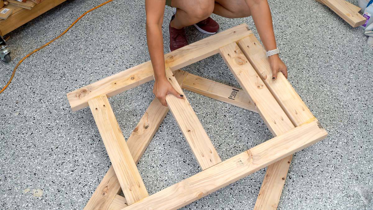 Woman putting two leg frames for the diy small mobile workbench on the garage floor