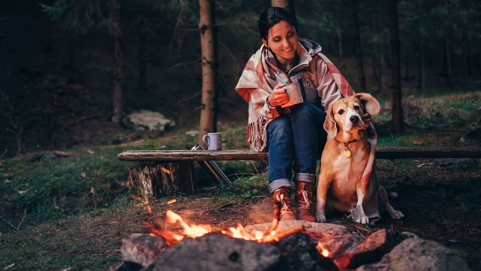 woman and dog sitting in front of a campfire