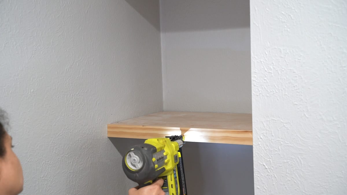 Woman attaching trim for the floating shelf in the nook using a nail gun