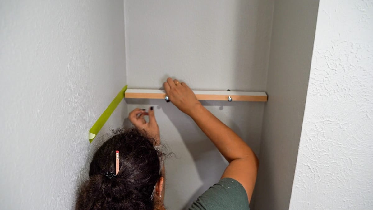woman attaching board to nook wall to install DIY floating shelves