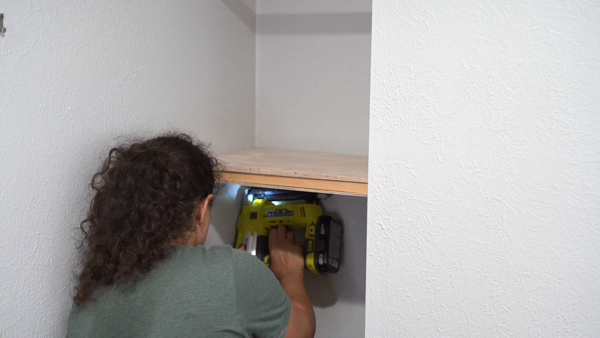 Woman attaching plywood for the floating shelf using a nail gun
