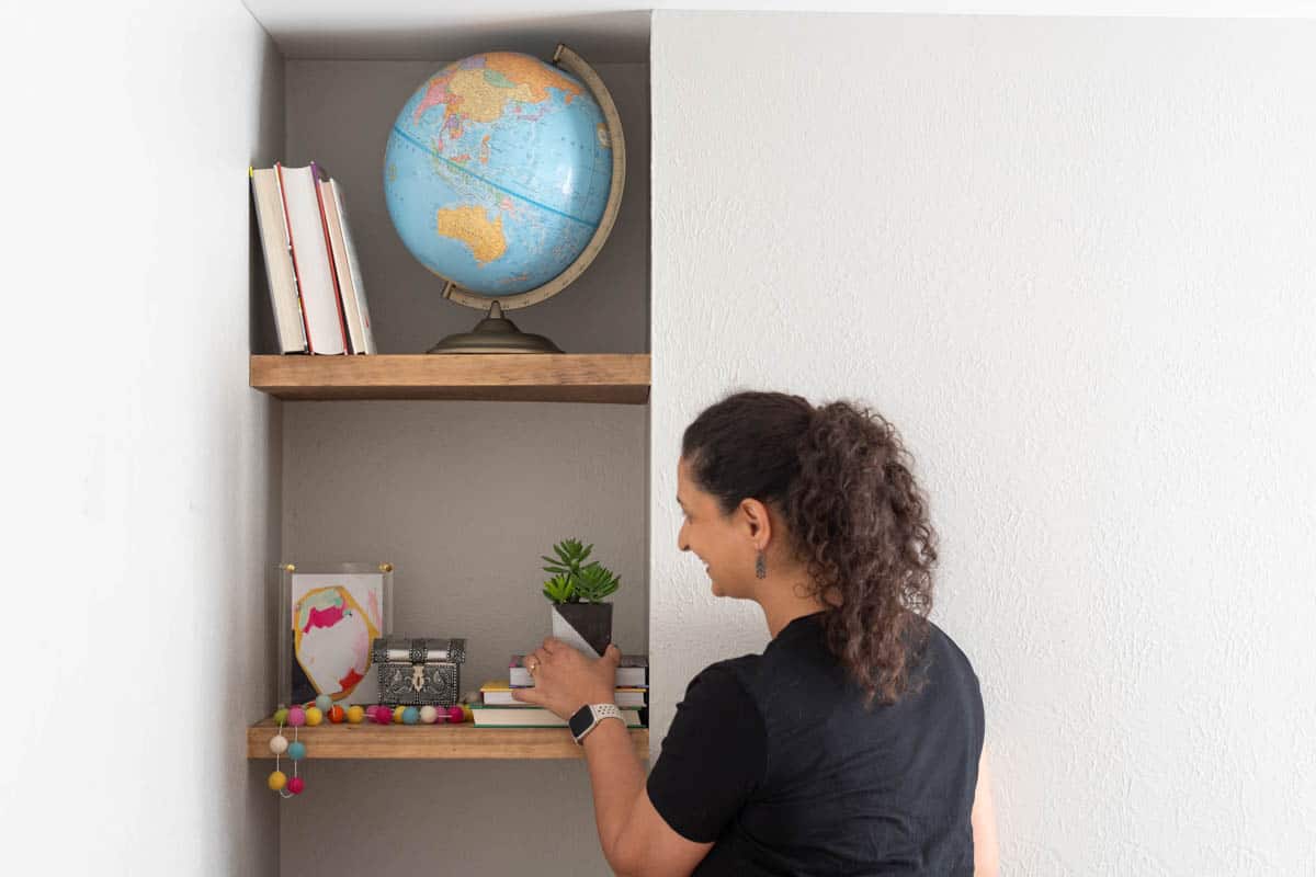 Anika adding items to wall shelves in a nook