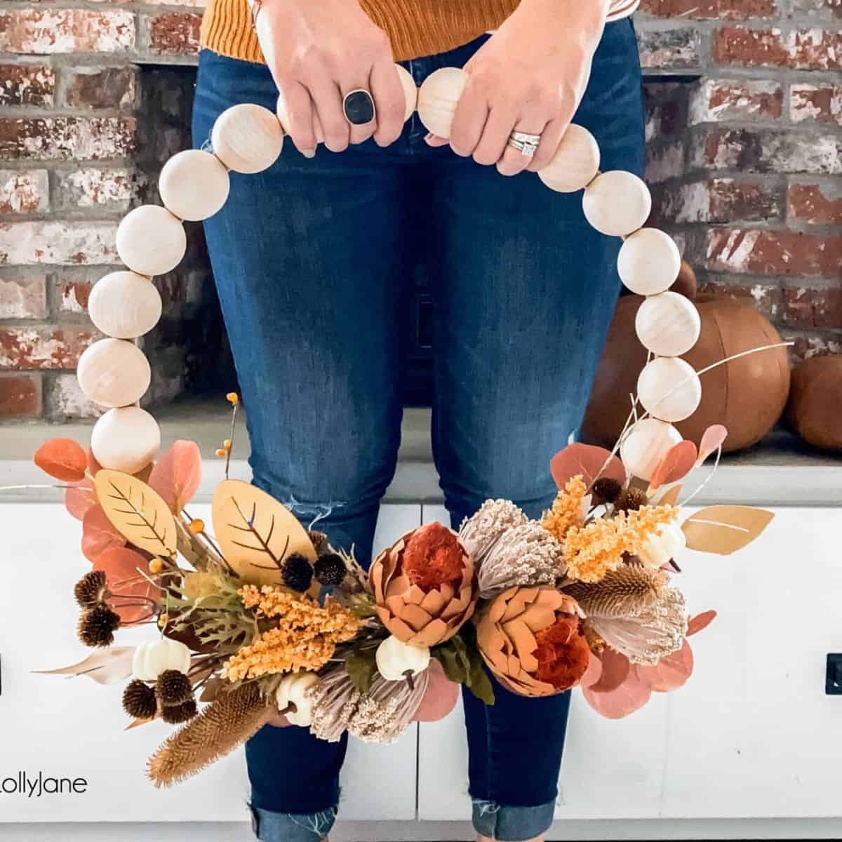 woman holding a DIY beaded wreath with fall greenery
