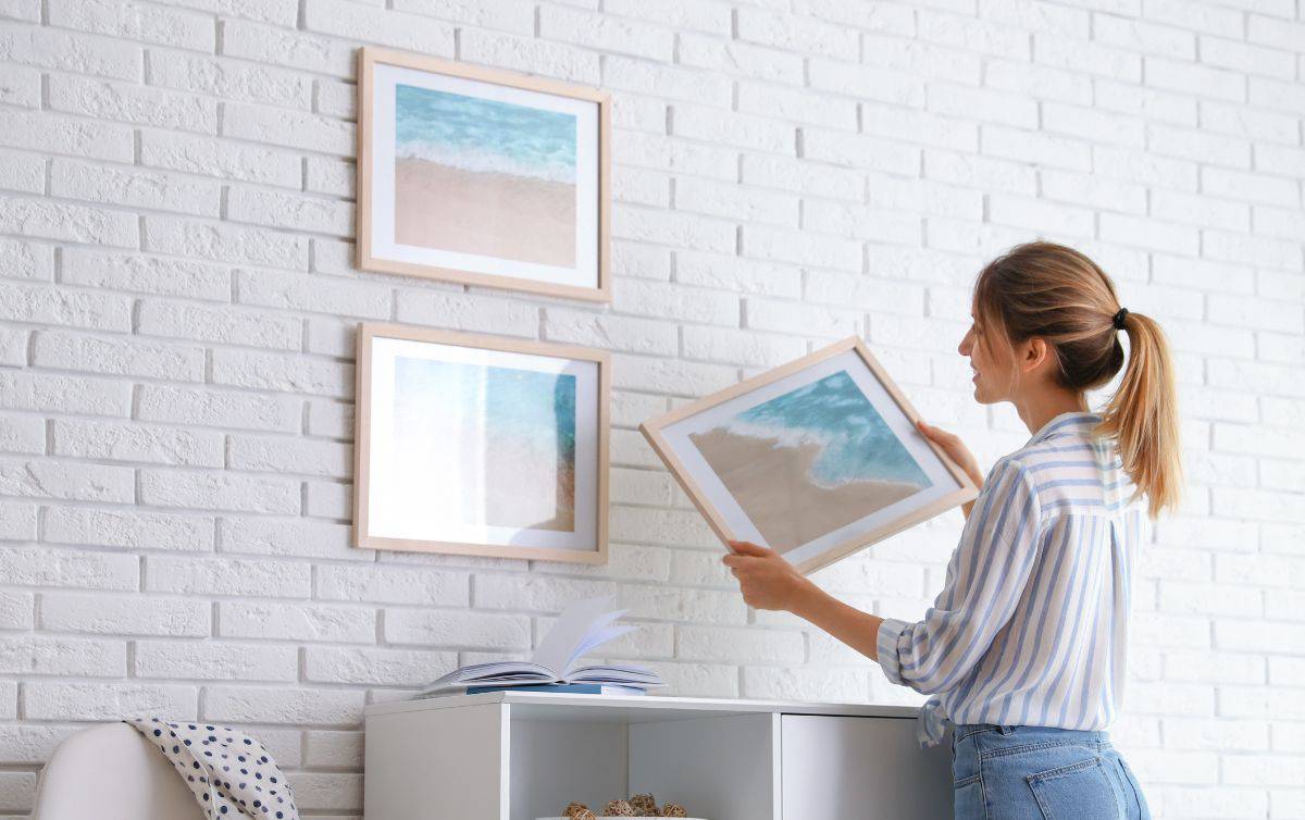 woman hanging a picture on a brick wall