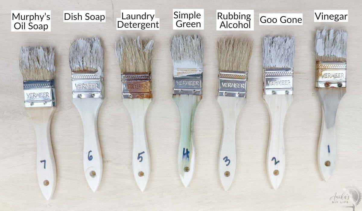 Brushes with dried paint cleaned by various liquids on a wood surface labeled with the cleaning solution used.