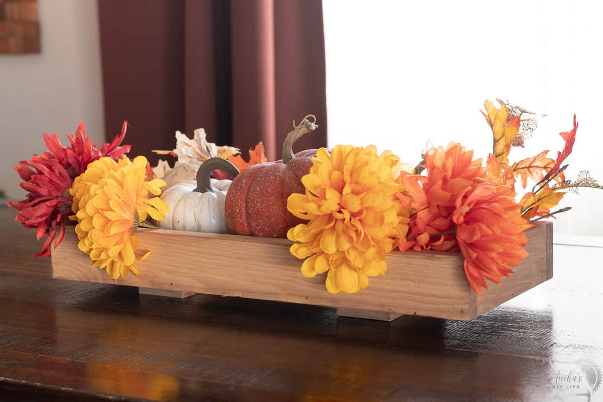 DIY wooden centerpiece with fall flowers and pumpkins on a dining table