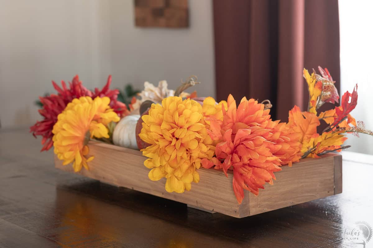 another angle of view of DIY wooden centerpiece decorated with fall flowers and pumpkins on a dining table