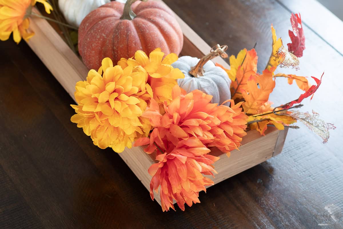DIY wooden centerpiece with fall flowers and pumpkins on a dining table