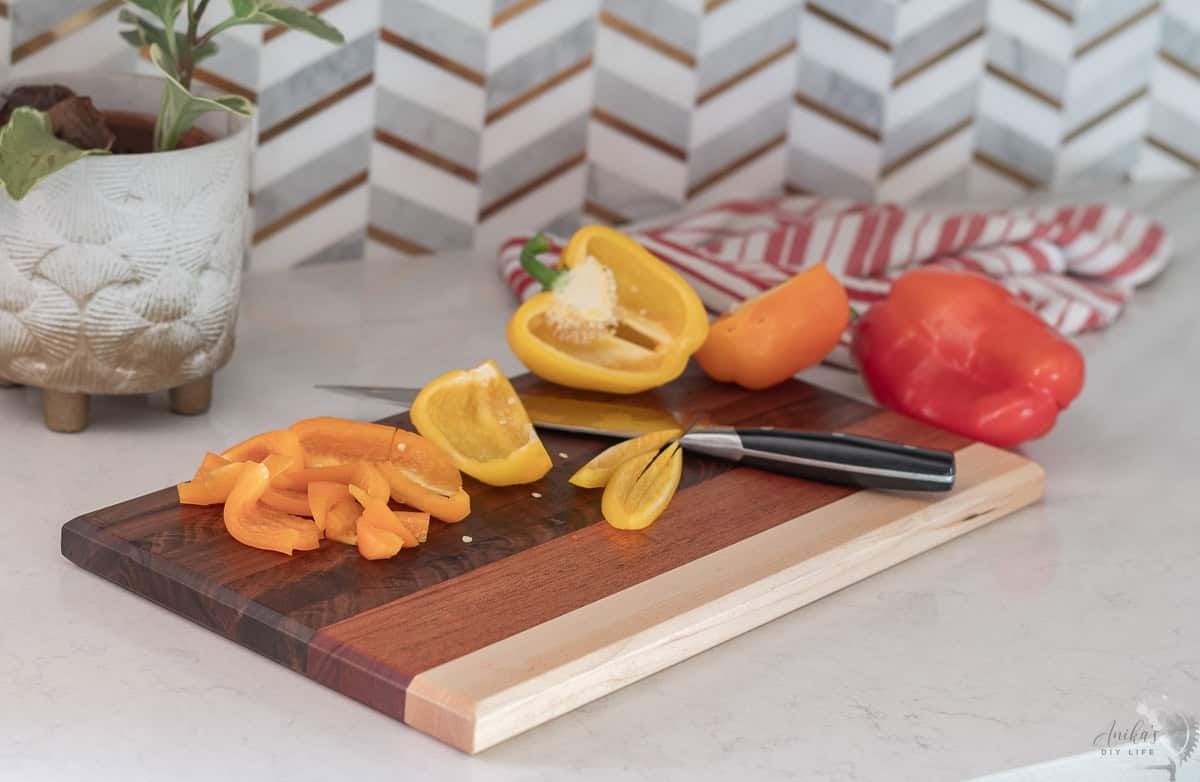 DIY cutting board with multiple wood types on a kitchen cocunter with bell peppers on it