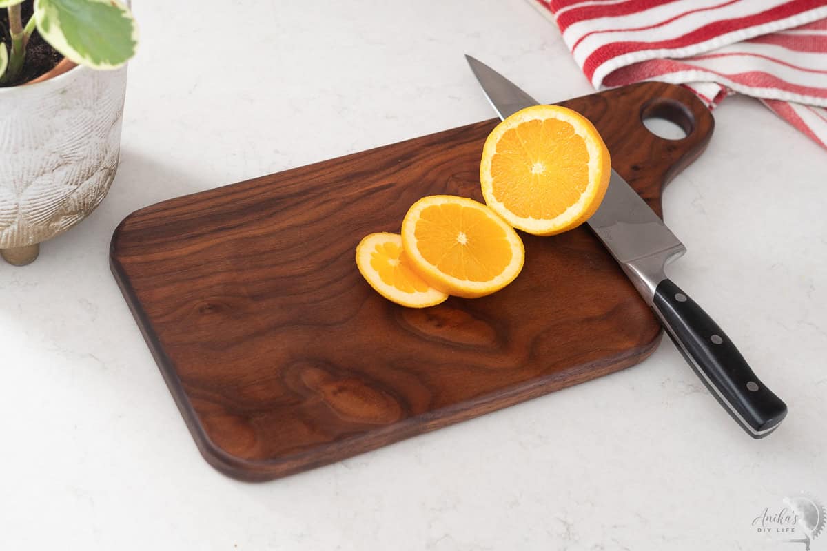 Walnut cutting board on white kitchen counter with sliced orange and knife