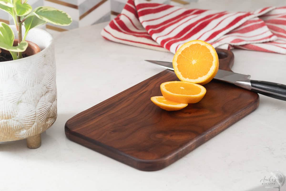 another angle view of the walnut cutting board on a white kitchen counter with sliced oranges and a knife