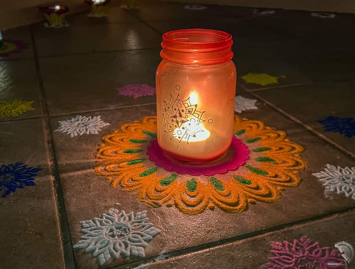 Reb glass jar with gold designs with tealight inside in the night surrounded by rangoli
