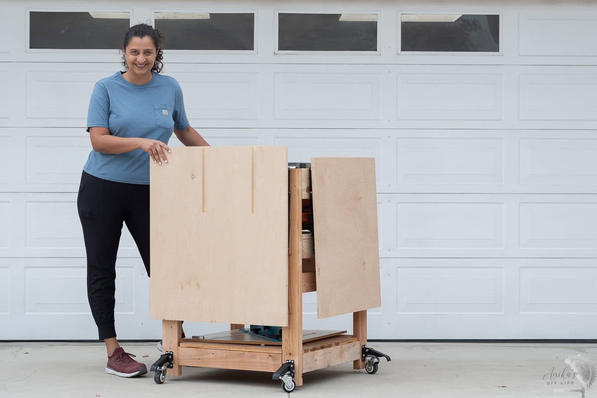 Anika standing in front of garage with a dIY table saw stand with folded outfeed table