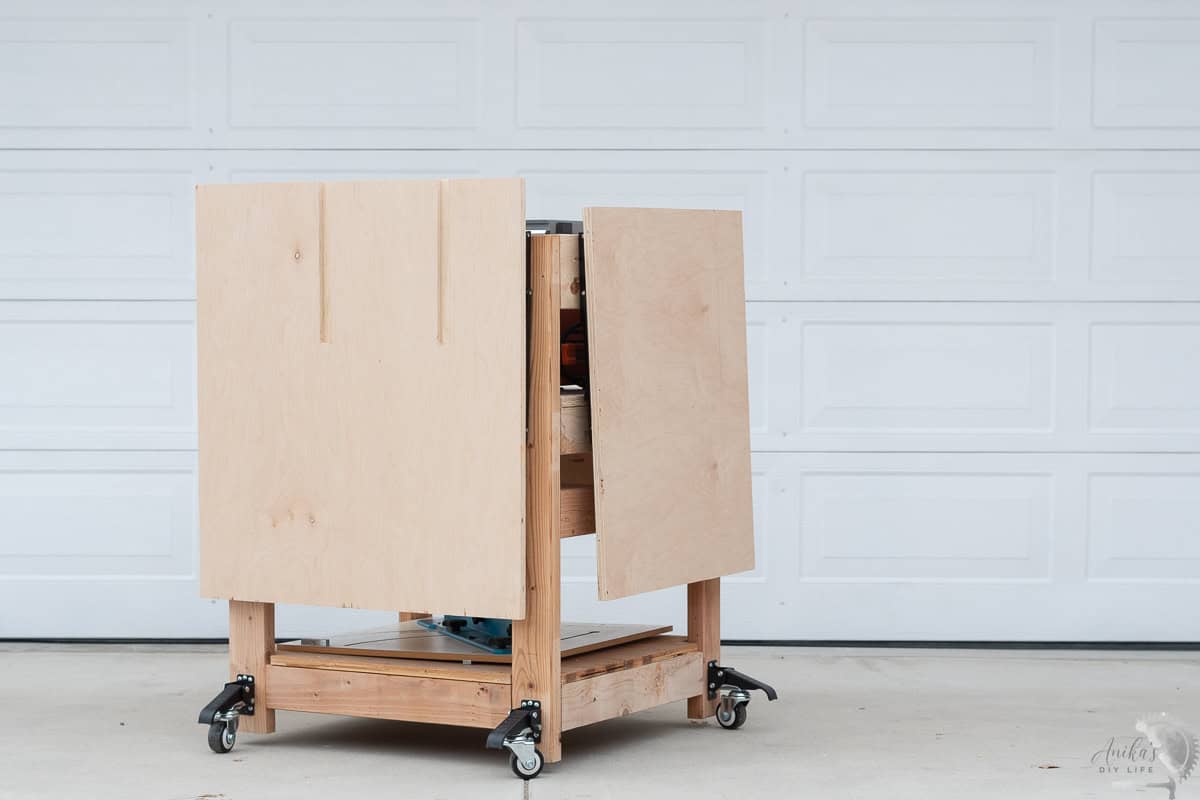 DIY Table saw stand with folding outfeed table, folded extension wing in the driveway in front of a garage