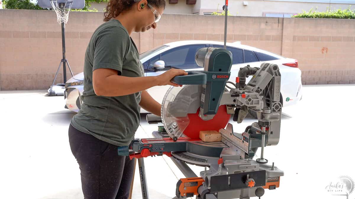 Anika cutting a 2x4 board using a miter saw in the driveway