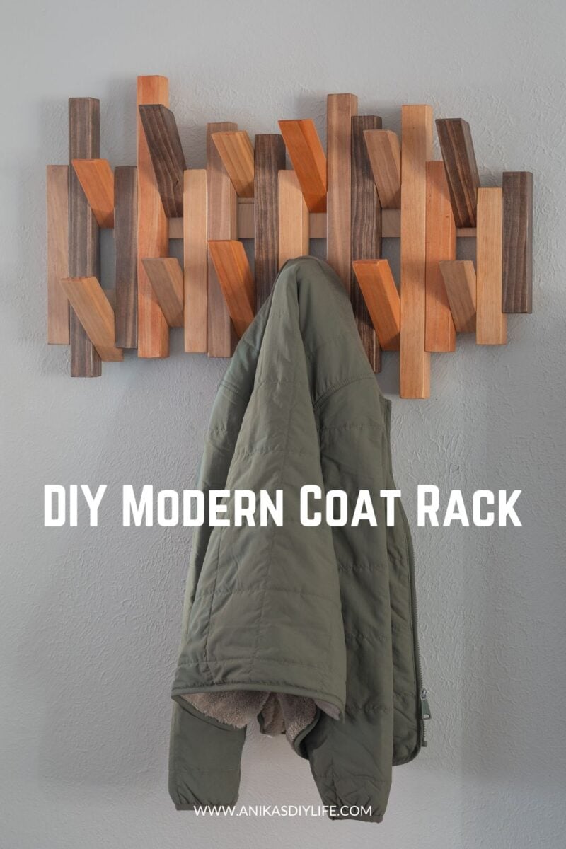 Modern diy coat rack on wall with some pegs open and a green jacket on one of the pegs. With text overlay stating DIY Modern Coat Rack