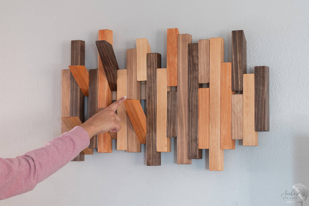 DIY Modern coat rack with colorful slats and a few pegs open. A woman is opening the pegs to hang a coat