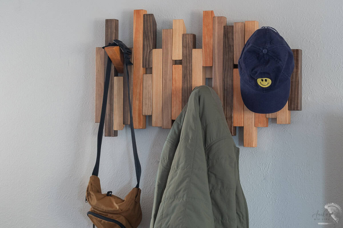 Modern diy coat rack on wall with some pegs open and a green jacket, bag and a cap on the pegs