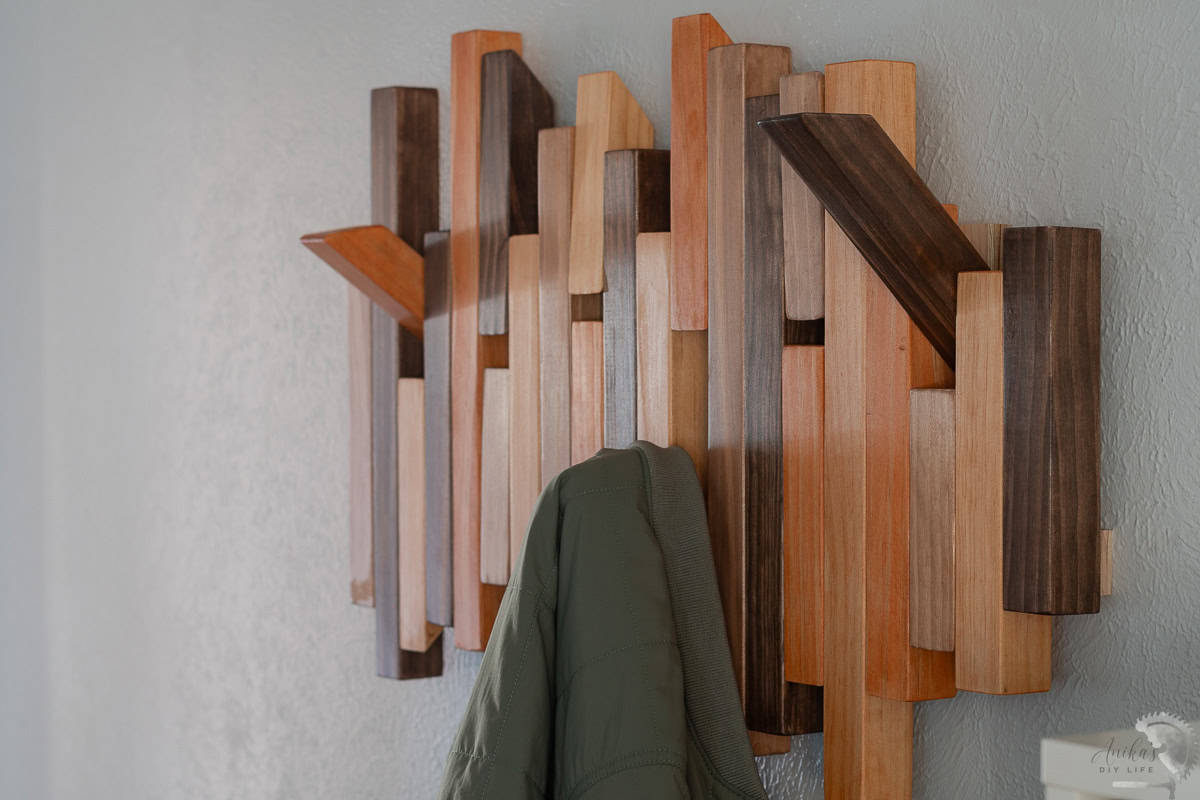 Modern diy coat rack on wall with some pegs open and a green jacket on one of the pegs.