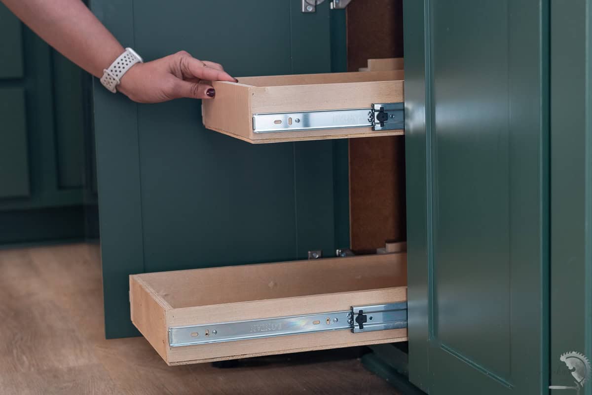Woman pushing the DIY pull-out shelves installed inside a deep green kitchen cabinet.