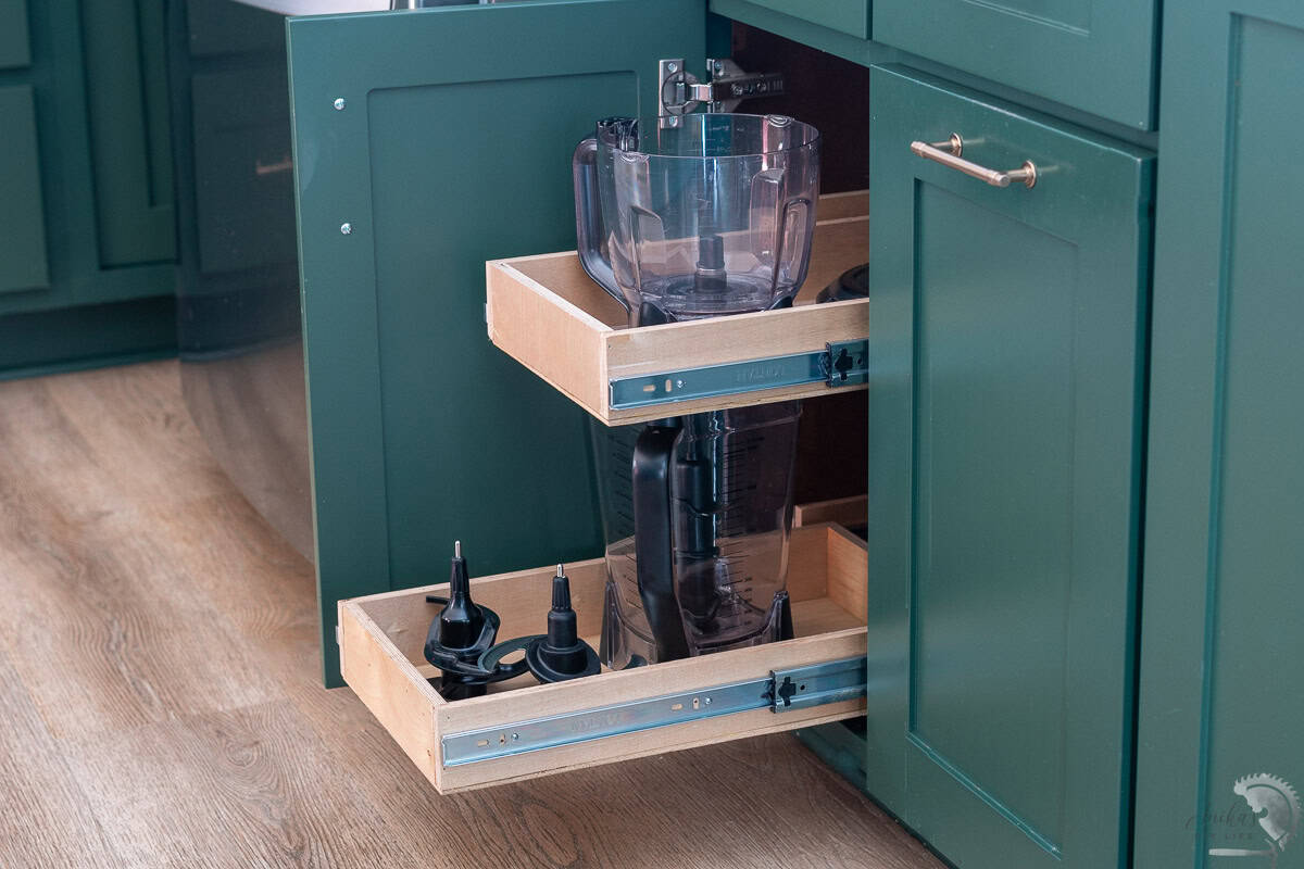 DIY pull-out shelves installed in a deep green kitchen cabinet, organizing blender jars and accessories. The sliding wooden drawers with metal slides make storage more accessible and efficient