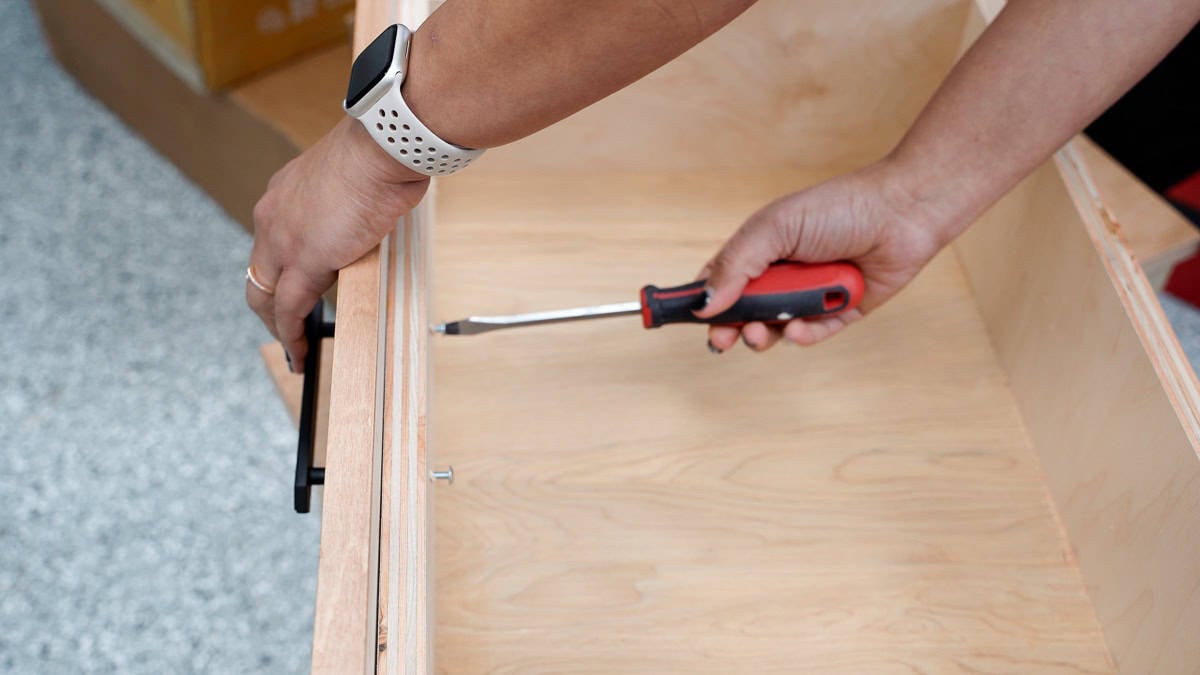 Attaching the drawer pulls to the drawer using a screwdriver