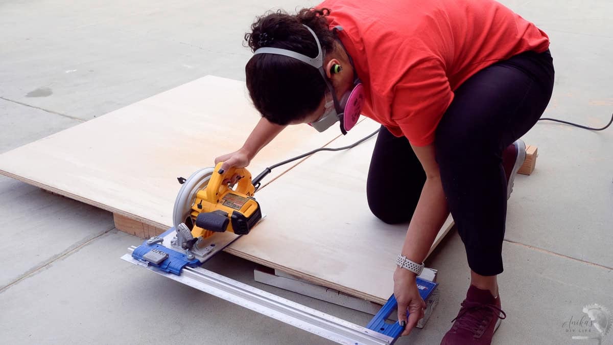 Anika cutting plywood for the diy dresser using a circular saw and kreg rip cut on the ground