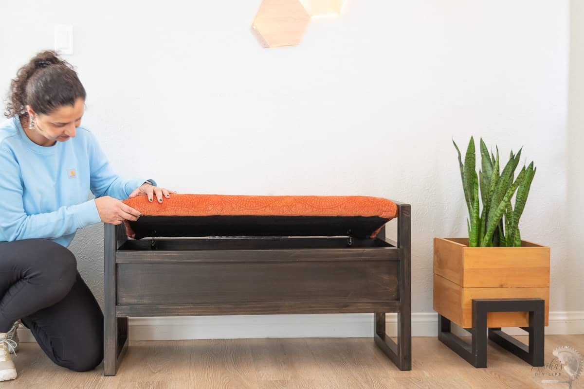 Anika opening the top of the diy upholstered storage bench to reveal the storage