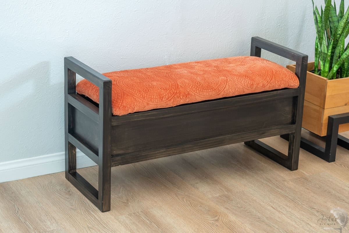 DIY upholstered storage bench with orange upholstery and black stain next to a plant