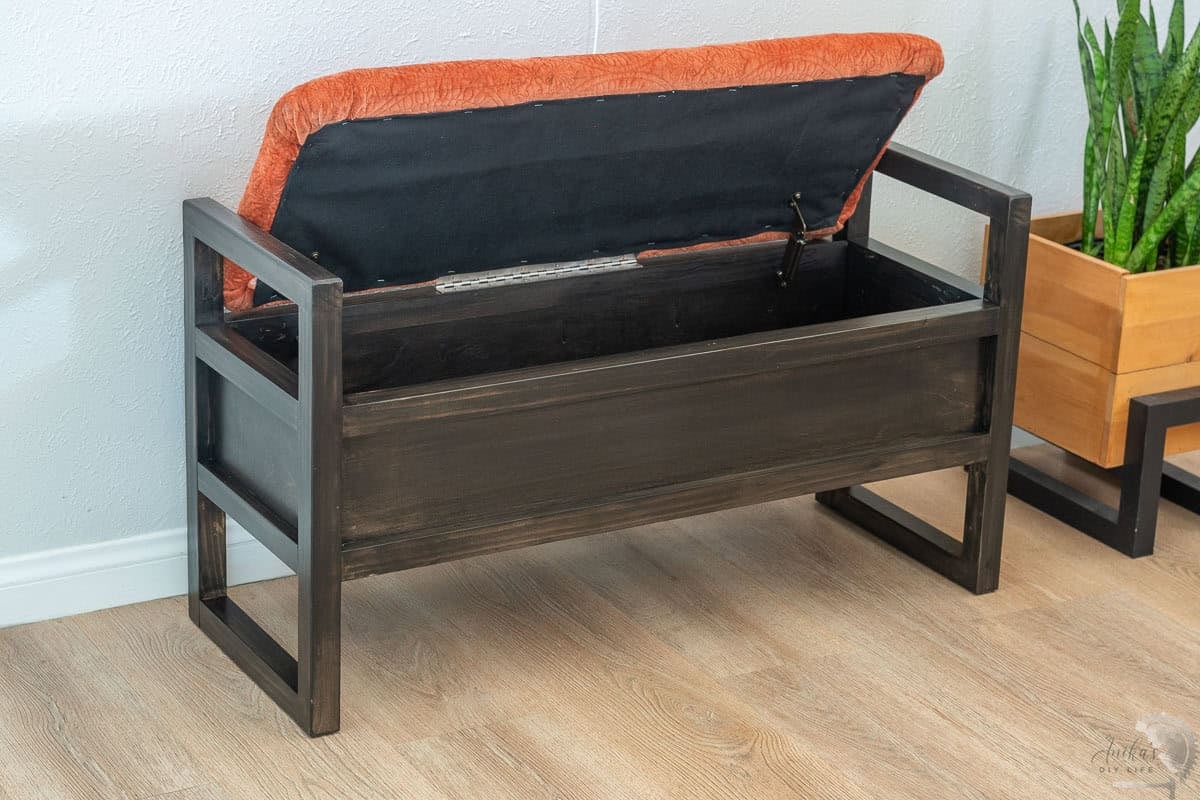 DIY upholstered storage bench with orange upholstery and black stain with the top open showing the storage space.
