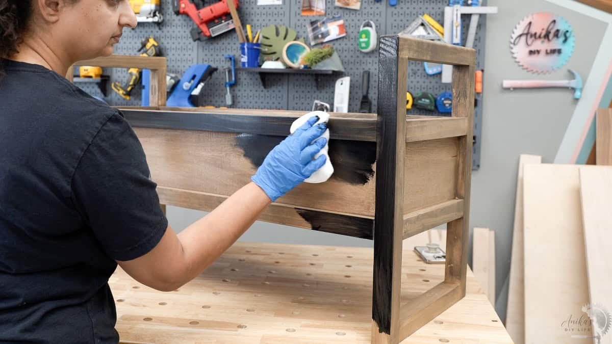 Anika applying black stain to the diy storage bench