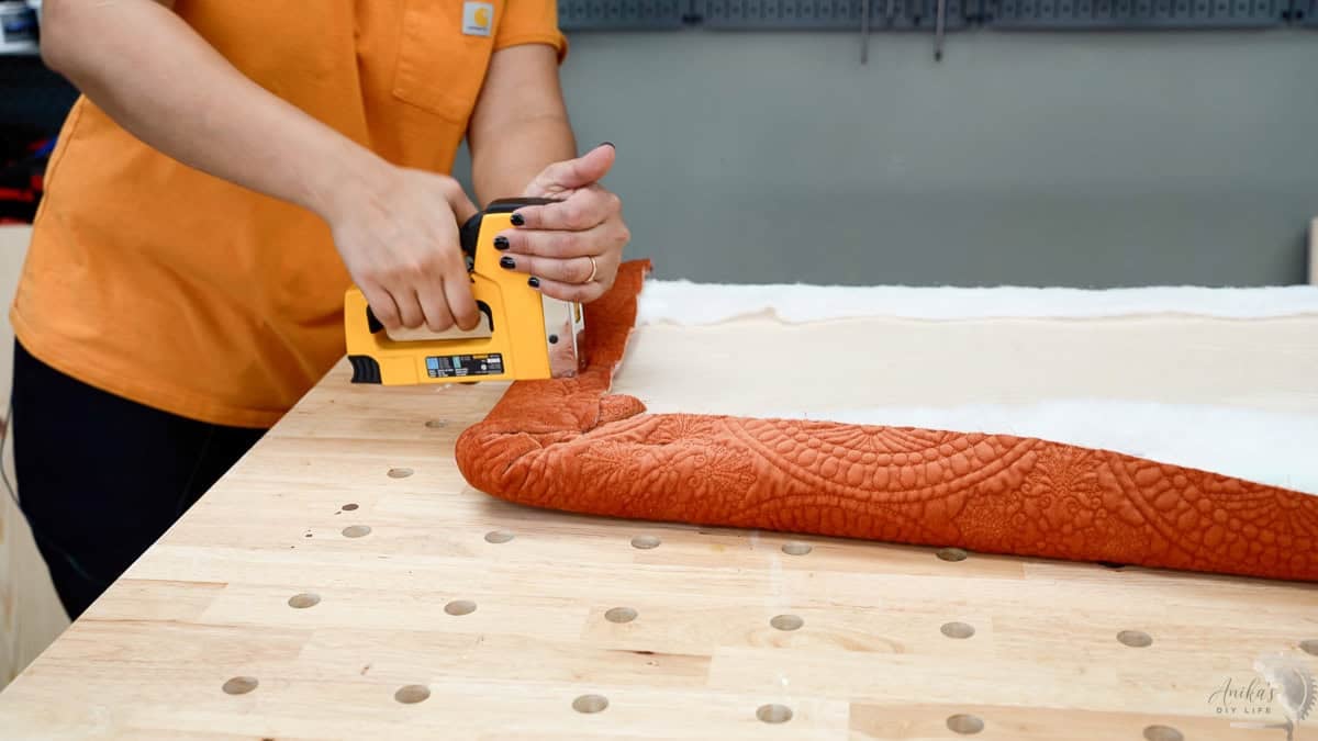 woman attaching orange upholstery fabric to plywood with a staple gun