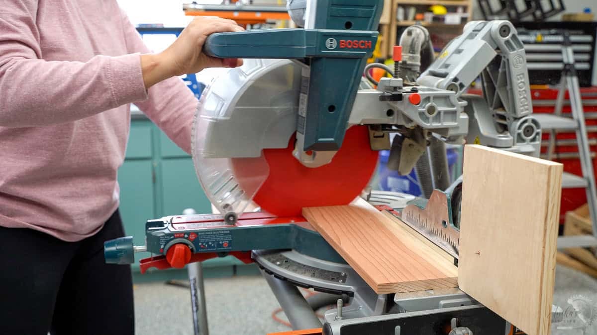 woman cutting a redwood 1x6 board on a miter saw with a stop block