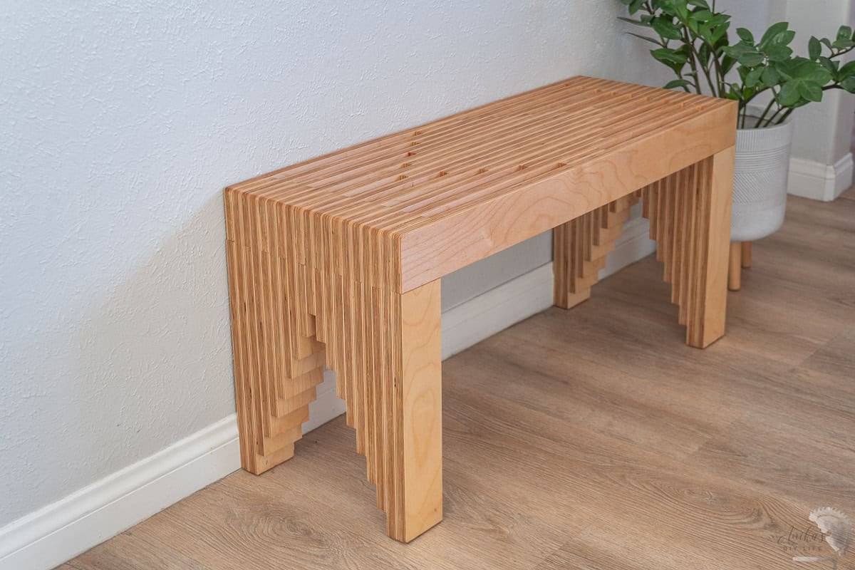 stacked plywood bench in front of a gray wall with plant next to it
