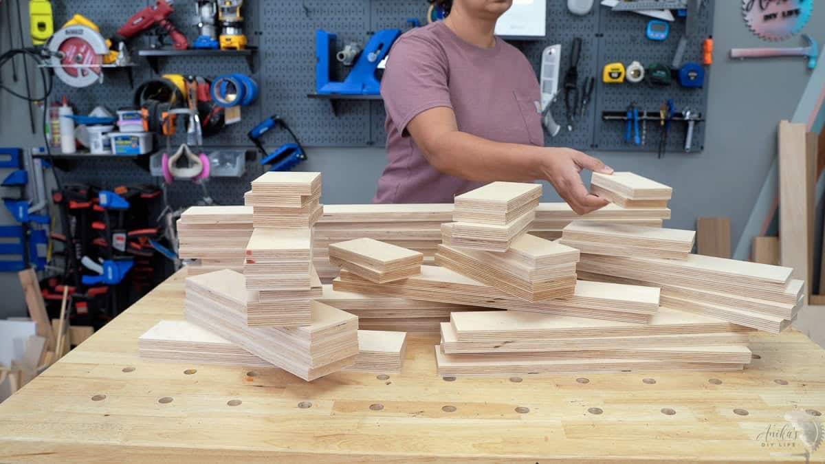 Anika stacking pieces of cut plywood for the diy plywood bench project on the workbench in a workshop