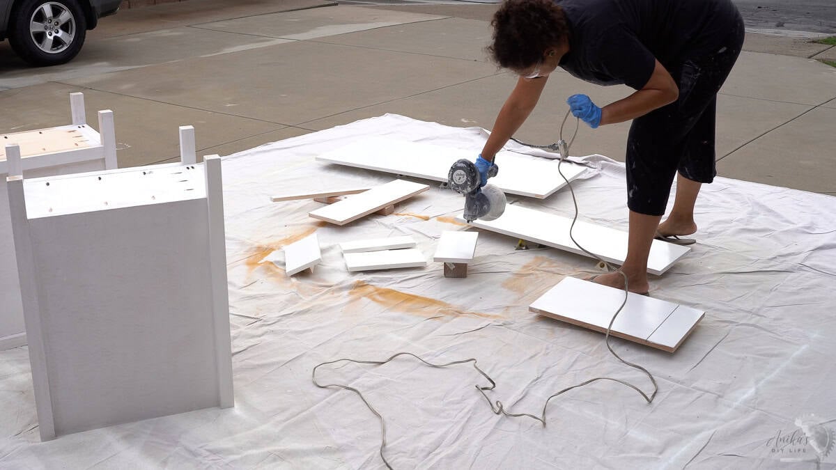 Anika painting parts of the desk with a paint sprayer in the driveway